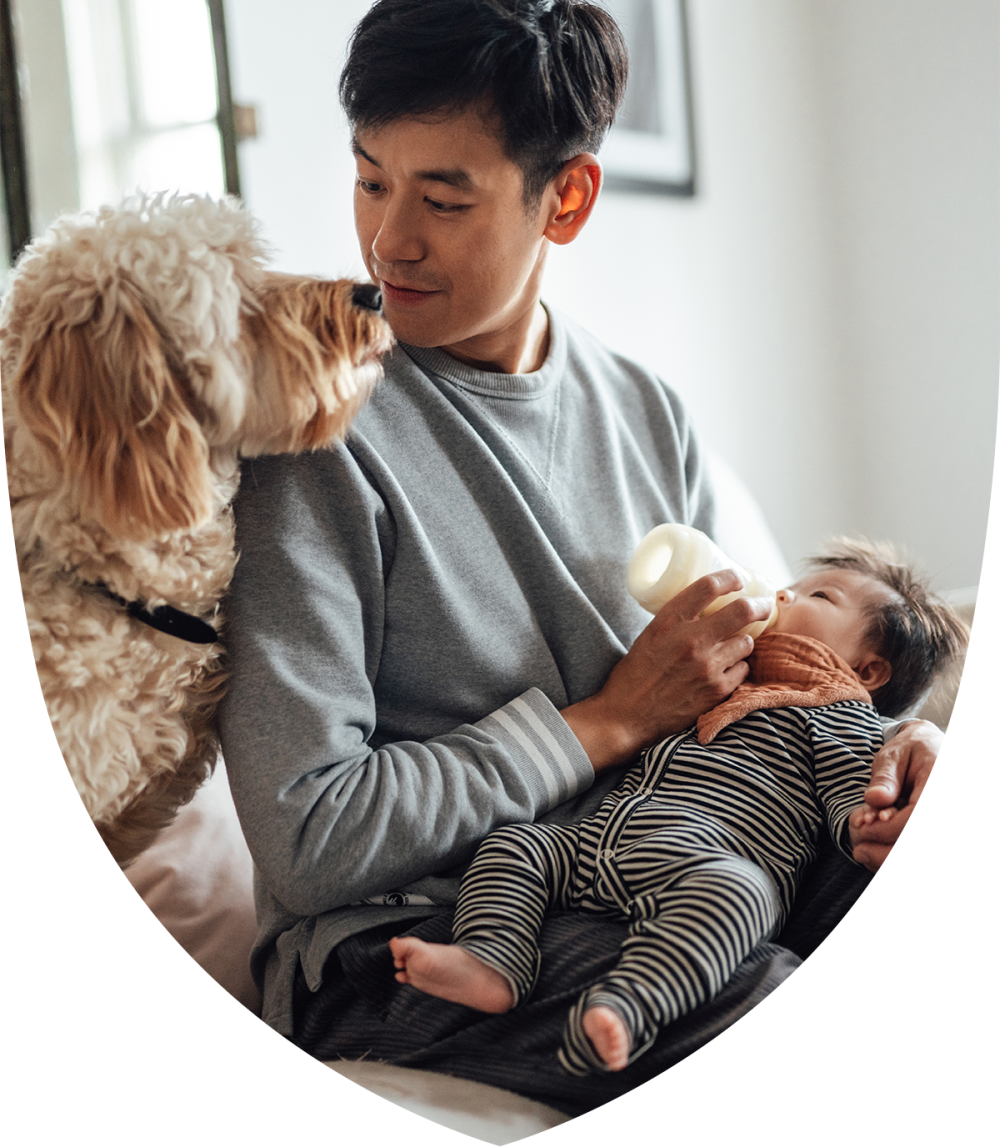 A man holding a baby and a dog over his shoulder