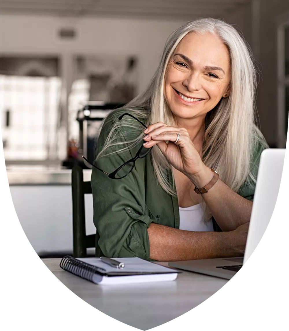 Close up of a woman holding her glasses and sitting at a laptop