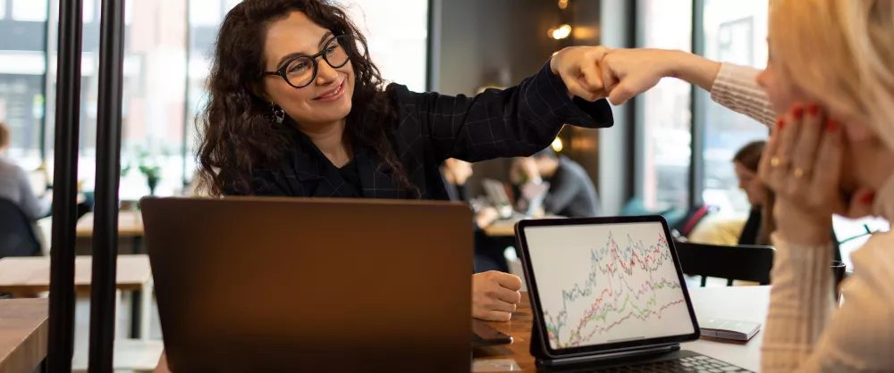 Two women fist bumping over laptops