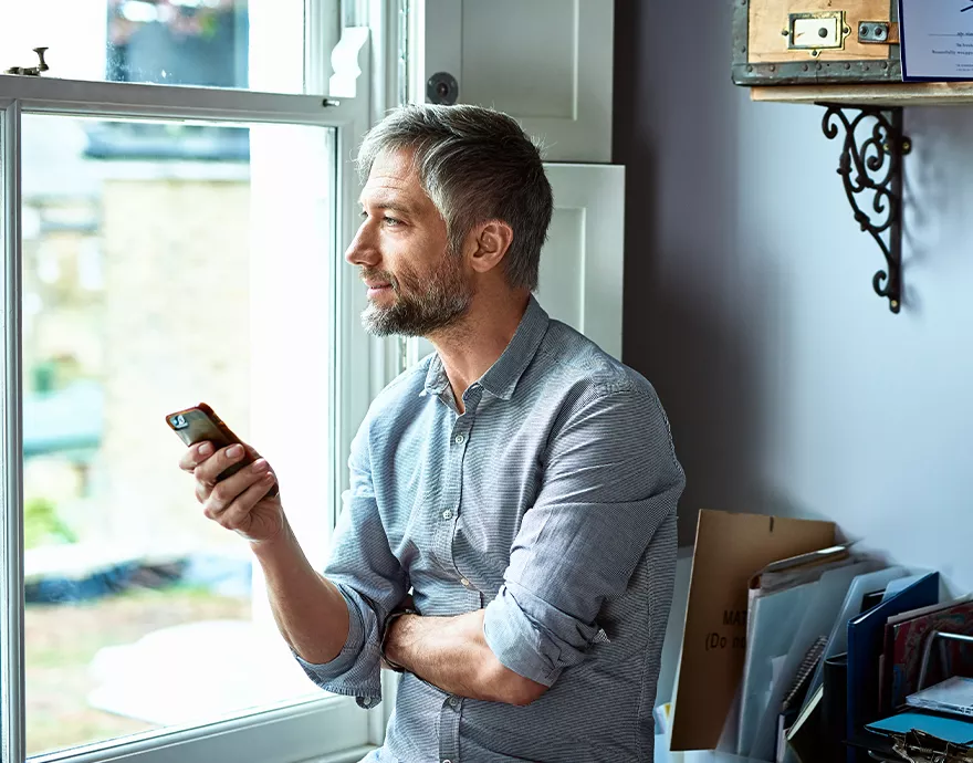 Middle aged man looking out the window while on his phone