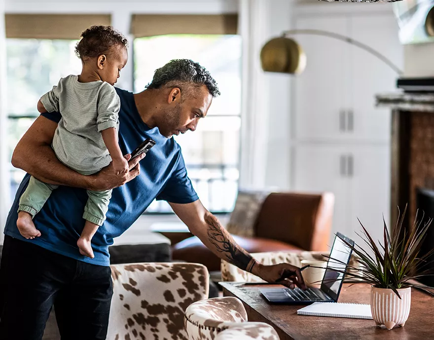 Father holding his son while browsing on his laptop