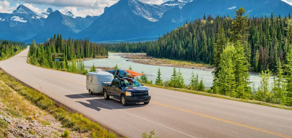 A pickup truck with a trailer driving through a scenic mountain road